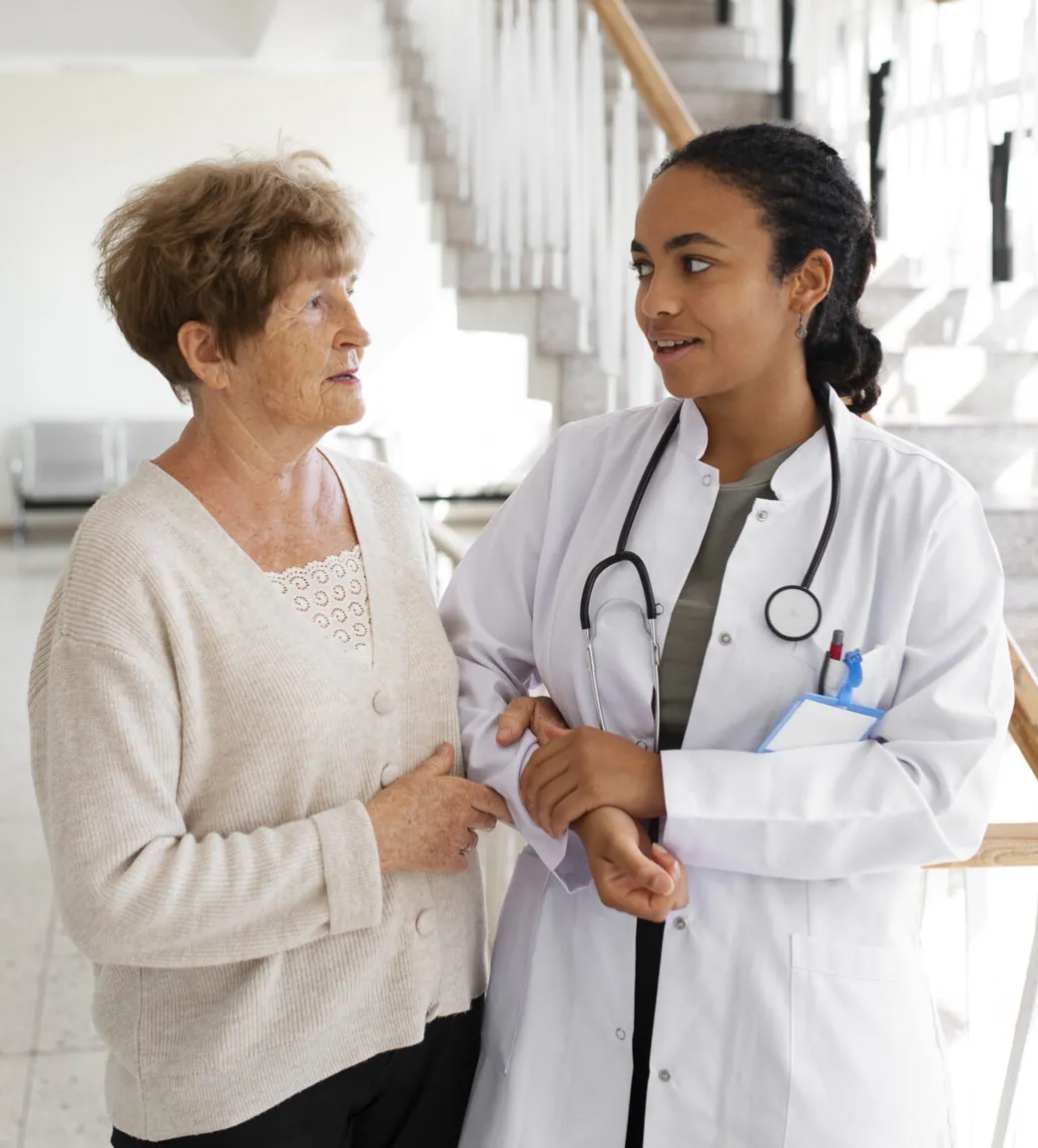 Médica de jaleco conversando com uma paciente idosa no corredor de um hospital